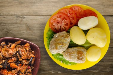 Sarı tabakta patates ve sebze salatası manzaralı pirzola. Kahverengi ahşap arka planda patatesli pirzola