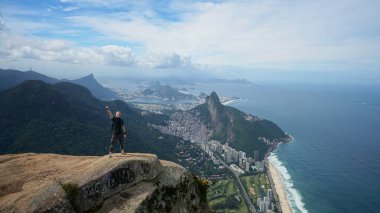 Brezilya 'daki Rio de Janeiro manzarasına panoramik hava manzaralı Pedra da Gavea dağının tepesindeki mutlu gezgin.. 