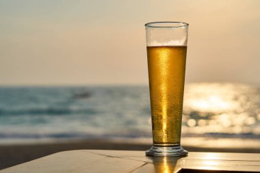 Gün batımında soğuk bira, arka planda deniz ve plaj..
