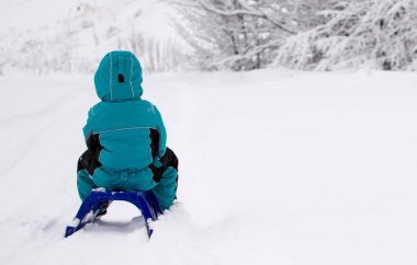 Küçük çocuk kızağını bekliyor. Tamamen beyaz, kış mevsimi. Dağdaki kış manzarası.