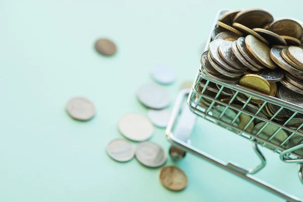 Carrinho de compras cheio de moedas sobre o fundo verde — Fotografia de Stock