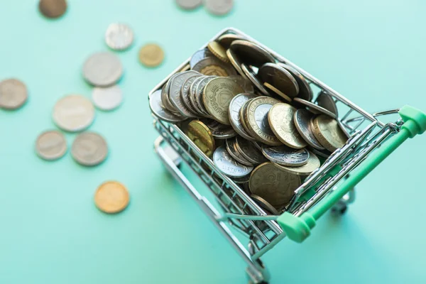 Shopping cart full of coins over the green background — Stock Photo, Image