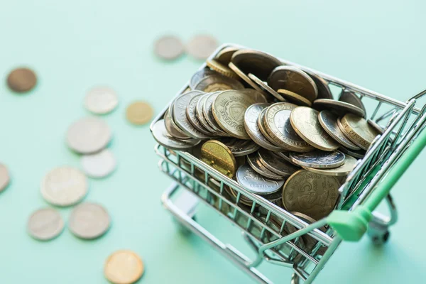 Shopping cart full of coins over the green background — Stock Photo, Image