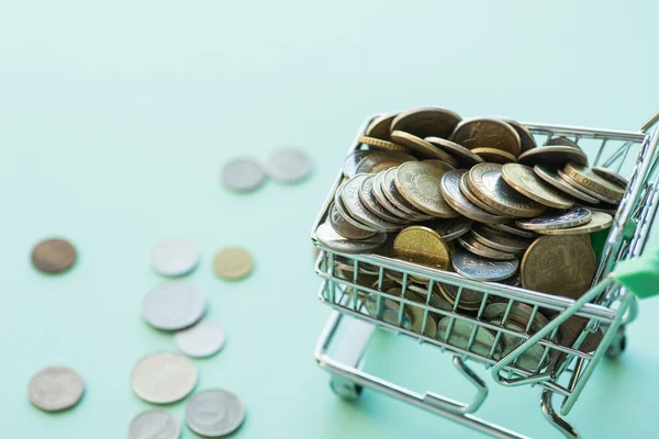 Shopping cart full of coins over the green background — Stock Photo, Image