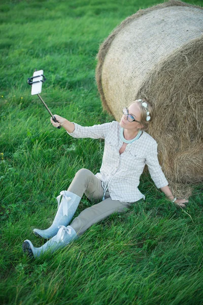 Beautiful young woman making a selfie on the grass in the meadow — Stock Photo, Image