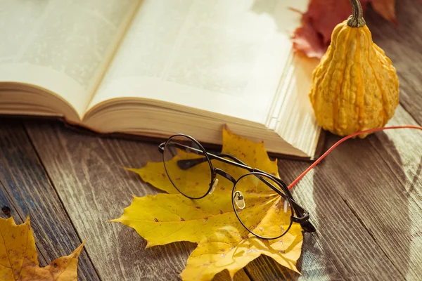 Eye glasses with book and autumn leaves on table — Stock Photo, Image