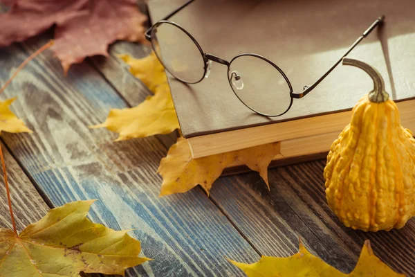 Eye glasses with book and autumn leaves on table — Stock Photo, Image