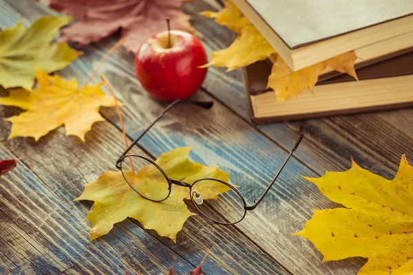 Gözlükleri ile kitap ve sonbahar yaprakları masaya