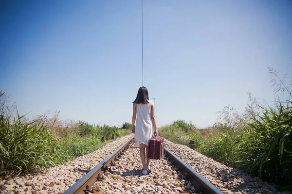 Donna sui binari ferroviari con una valigia retrò — Foto Stock