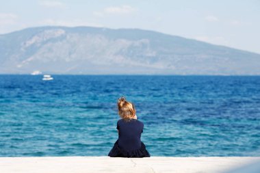 Mavi denizi ve beyaz taşlar ve mavi elbiseli oturma ve manzarayı küçük kız