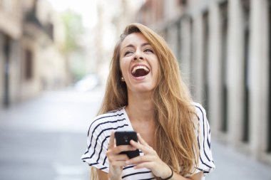 Gülümseyen kadın bir smartphone kullanarak sokakta yürürken