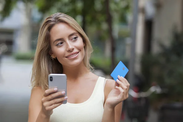 Mujer Sonriente Sosteniendo Tarjeta Crédito Teléfono Inteligente Pensando Mirando Lado —  Fotos de Stock