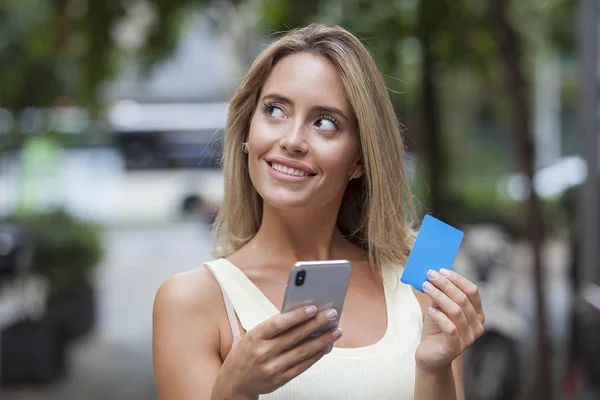 Mujer Sonriente Sosteniendo Tarjeta Crédito Teléfono Inteligente Pensando Mirando Lado — Foto de Stock