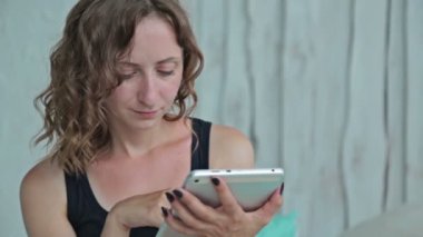 Genç kıvırcık kadın yatakta tablet pc ile oturuyordu. Dolly vurdu
