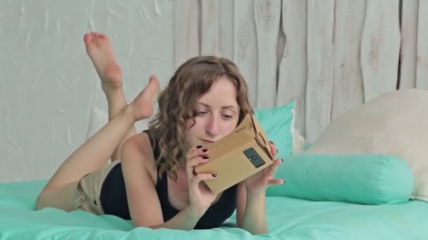 Mulher encaracolada usando óculos de realidade virtual e deitada na cama. Dolly atirou — Vídeo de Stock