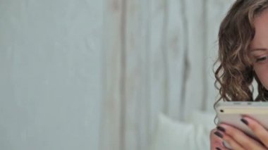 Genç kıvırcık kadın yatakta tablet pc ile oturuyordu. Dolly vurdu