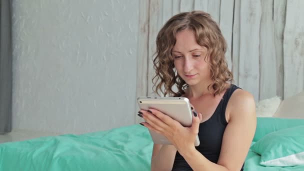 Junge lockige Frau sitzt mit Tablet-PC im Bett — Stockvideo