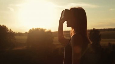 Kadın bir sanal gerçeklik gözlük ormanda günbatımında kullanır