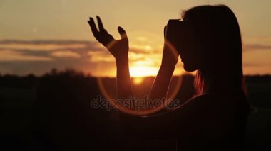 Kadın bir sanal gerçeklik gözlük ormanda günbatımında kullanır