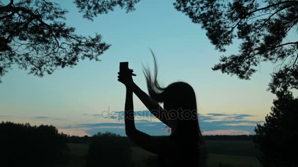 Silhouet van een jonge vrouw die selfie met haar telefoon na zonsondergang — Stockvideo