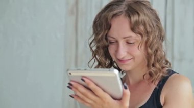 Tablet pc ile yatakta oturan genç kıvırcık kadın.