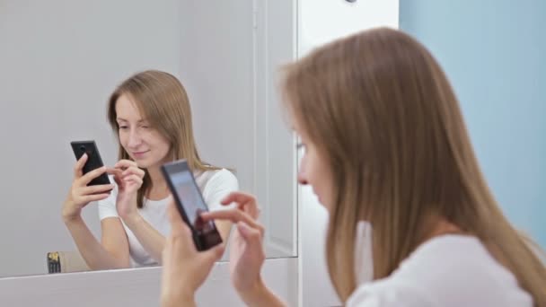 Жінка за допомогою смартфона сидить перед дзеркалом — стокове відео