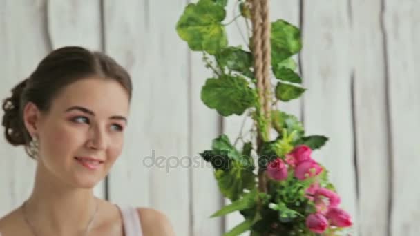Mulher bonita com maquiagem e penteado em um balanço decorado com flores . — Vídeo de Stock