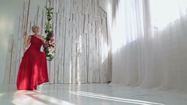 Jolie, jeune et sensuelle femme en robe rouge sur une balançoire décorée de fleurs — Video