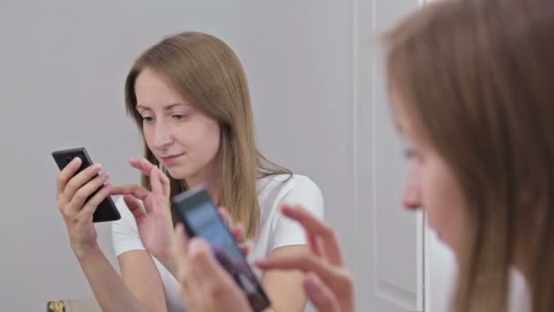 Frau sitzt mit Smartphone vor Spiegel — Stockvideo