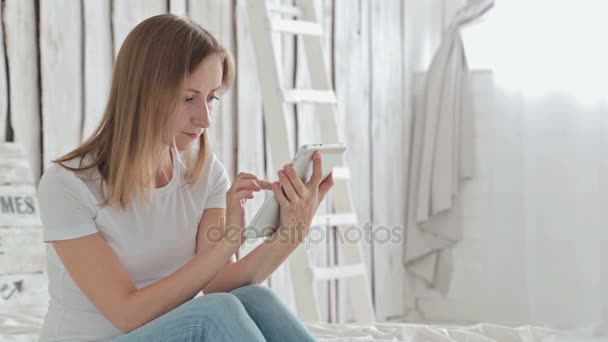 Mujer joven sentada en la cama con la tableta PC — Vídeo de stock