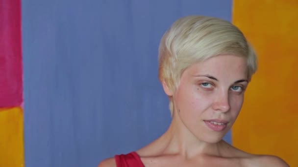 Hübsche, junge, blonde Frau in rotem Kleid ohne Make-up, die in die Kamera schaut — Stockvideo