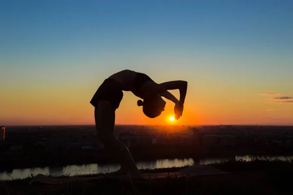 Woman practicing yoga at sunset - drop back, wheel pose