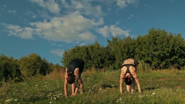 Sportovní muž a žena, která dělá Ashtanga Jóga v parku při západu slunce — Stock video