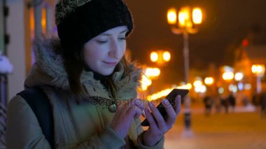 Smartphone şehirde geceleri kullanan genç güzel kadın