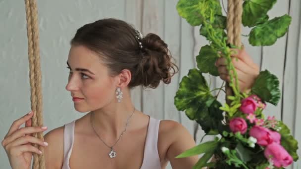 Vrouw met mooie make-up en kapsel op een schommel versierd met bloemen. — Stockvideo