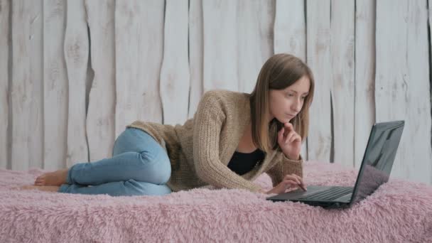 Жінка лежить на ліжку і використовує ноутбук — стокове відео