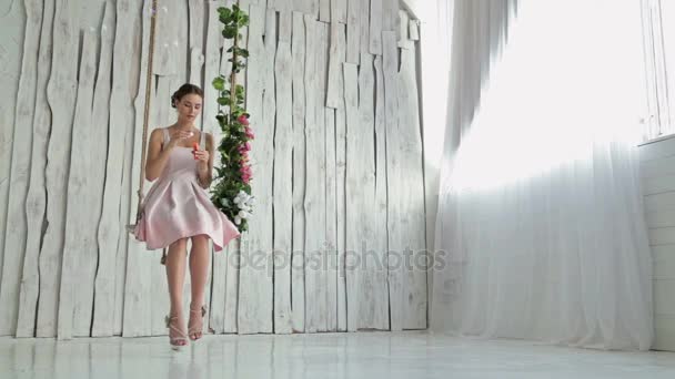 Sensual woman with make-up on a swing decorated with flowers blowing bubbles — Stock Video