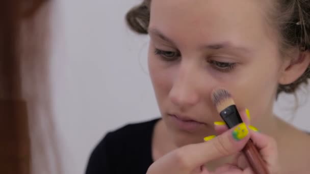 Dois tiros. Maquiagem artista aplicando base tonal líquida no rosto da menina adolescente — Vídeo de Stock