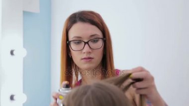 Genç kadın güzel için saç modeli yapıyor ve saç spreyi kullanarak Kuaför