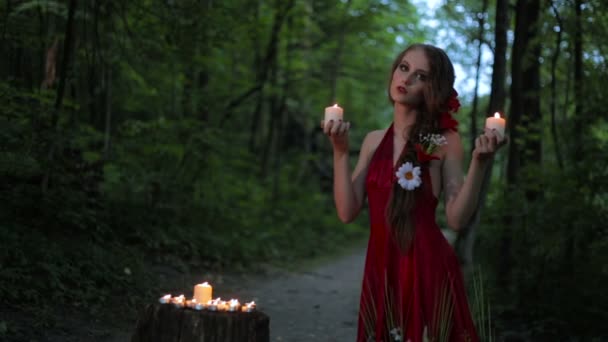 Menina incomum com maquiagem criativa segurando duas velas em chamas na floresta escura — Vídeo de Stock