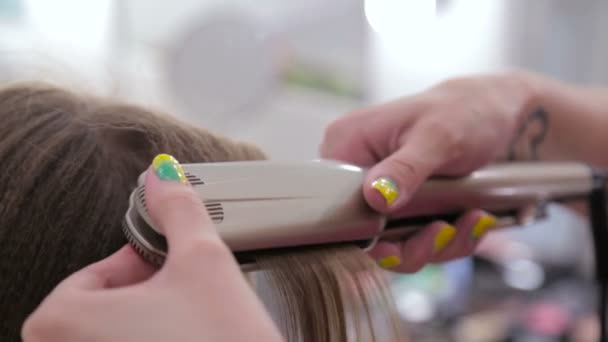 Парикмахер с помощью выпрямителя на длинных волосах клиента в парикмахерской — стоковое видео