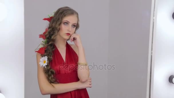 Необычная девушка с креативным макияжем в платье, смотрящая на свое отражение в зеркале — стоковое видео