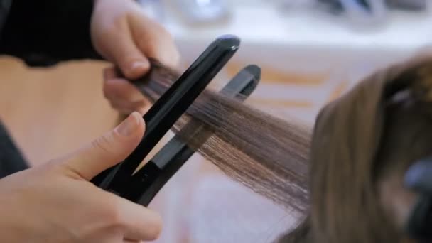 Coiffeur utilisant redresseur sur les cheveux longs du client dans le salon de coiffure — Video