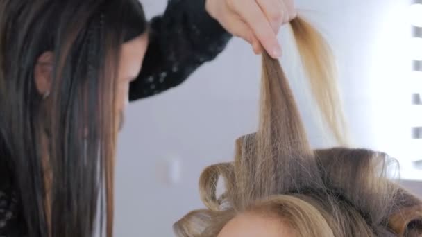 Professional hairdresser doing hairstyle for young pretty woman - making curls — Stock Video