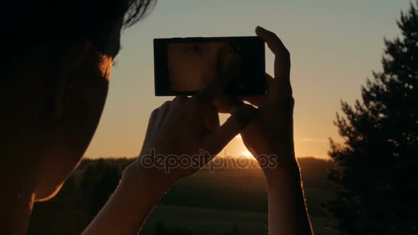 Silueta de mujer tomando fotos del atardecer con smartphone — Vídeos de Stock