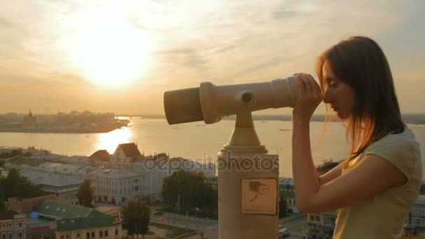 Young woman looking through tourist telescope, exploring city at sunset — Stock Video