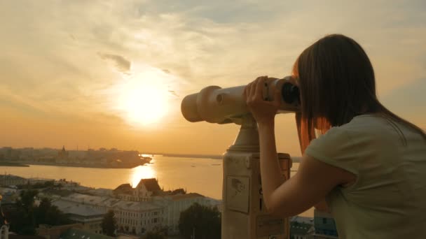 Mujer joven mirando a través del telescopio turístico, explorando la ciudad al atardecer — Vídeos de Stock