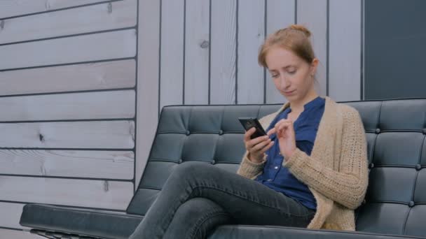 Young woman using smartphone on couch in modern office — Stock Video