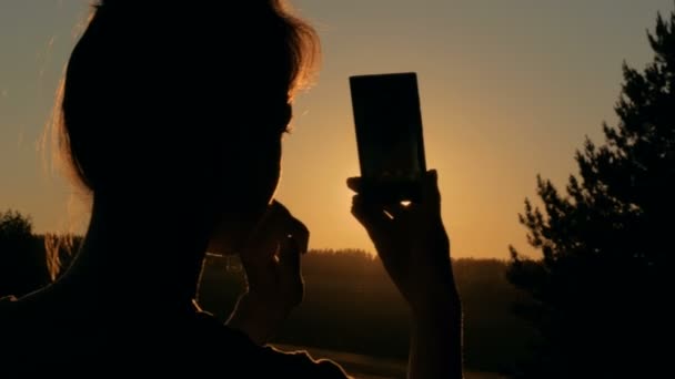 Silueta de mujer tomando fotos del atardecer con smartphone — Vídeos de Stock