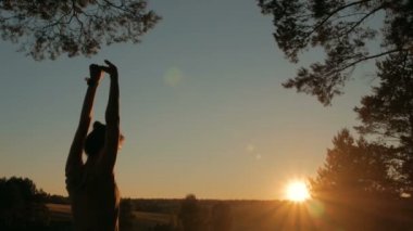 Gün batımında orman gökyüzüne doğru uzanan genç kadın